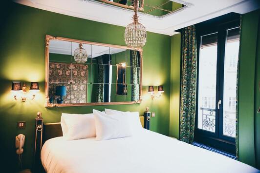 Hotel bed with chandelier and mirror.